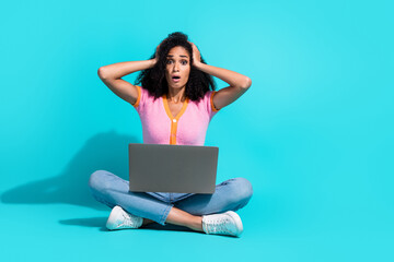 Surprised young woman holding laptop with a turquoise background, expressing astonishment with...