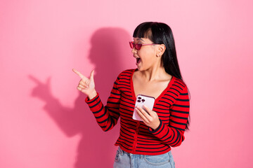 Obraz premium Cheerful young woman holding phone and gesturing excitedly against pink background