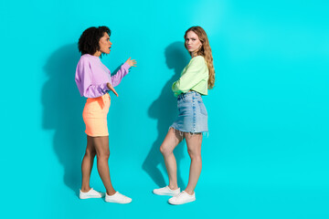 Two stylish females in vibrant outfits interact against a turquoise background, showcasing...