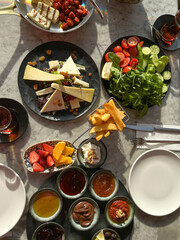 A vibrant Turkish breakfast spread with fresh vegetables, cheeses, fruits, and various spreads, beautifully arranged on a marble table under warm sunlight
