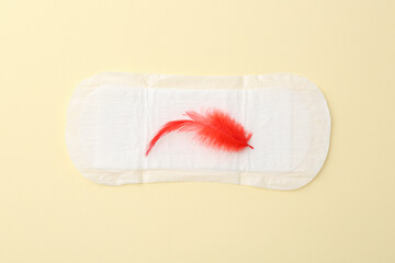 Menstrual pad with red feather on beige background, top view