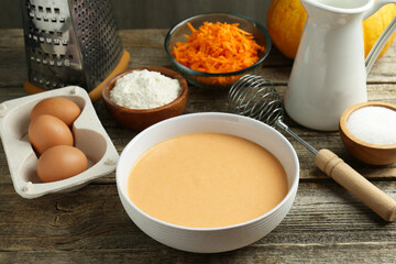 Bowl with dough and ingredients for pumpkin pancakes on wooden table