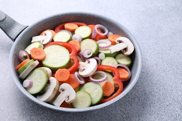 Frying pan with mix of fresh vegetables and mushrooms on grey table, closeup