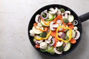 Frying pan with mix of vegetables and mushrooms on light grey table, top view. Space for text
