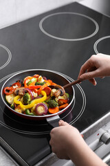 Woman cooking vegetables and mushrooms in frying pan on cooktop indoors, closeup