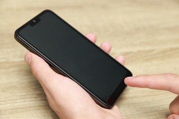 Man using smartphone with blank screen at wooden table, closeup