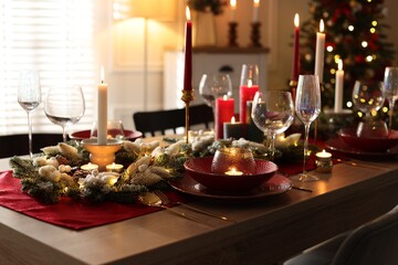 Christmas table setting with stylish dishware, glasses and burning candles in festive decorated room