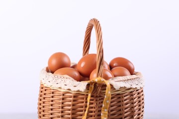 Wicker basket with fresh eggs on white background, closeup