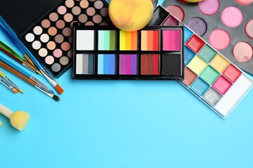 Bright face paints, brushes and sponges on light blue background, flat lay. Space for text