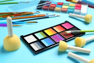 Bright face paints, brushes and sponges on light blue background