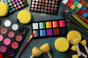 Bright face paints, brushes and sponges on color background, flat lay