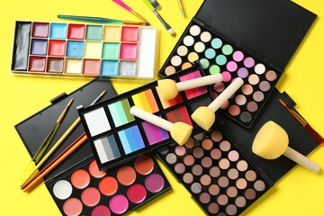 Face paints, tools and makeup products on yellow background, flat lay