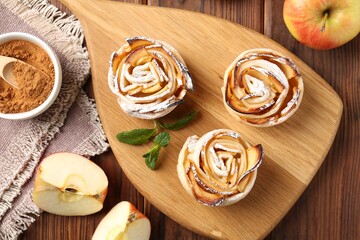 Tasty apple roses with powdered sugar served on wooden table, flat lay