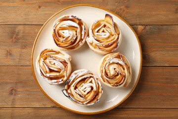 Tasty apple roses with powdered sugar on wooden table, top view