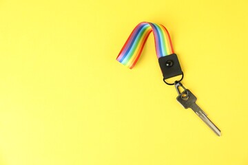 Key with keychain in LGBT colors on yellow background, top view. Space for text