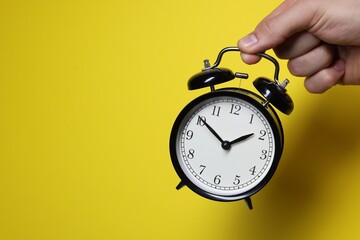 Man with alarm clock on yellow background, closeup. Space for text