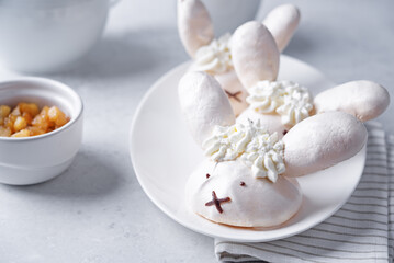 Meringue cake with apple filling and whipped cream on top in the form of funny rabbits in a plate