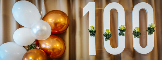 A festive 100 decoration with yellow flowers hangs against a beige curtain, accompanied by a gold...