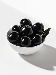Fresh black olives in a white bowl with a green leaf on a bright surface