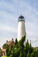White Lighthouse with Brick Buildings and Lush Greenery Under Blue Sky
