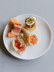 Gourmet tasting plate featuring seafood, fresh fruits, and a delicate egg garnish set on a neutral background