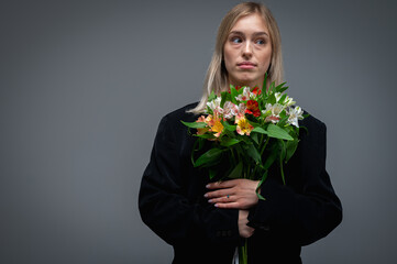 Portrait of a young woman with a bouquet of fresh spring flowers, smiling and excited. Studio shot with soft lighting and a neutral background that captures the emotions and natural beauty	
