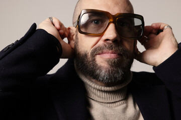 Obraz premium Close-up portrait of mature bald man with beard, wearing sunglasses posing confidently indoor.