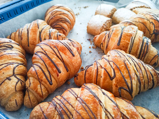 Freshly baked chocolate drizzled croissants in a bakery display case