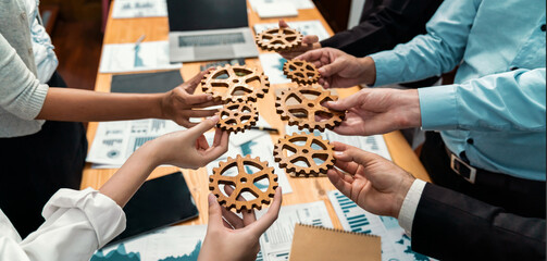 Group of multiracial business people joining gear wheels together over table as effective unity and...