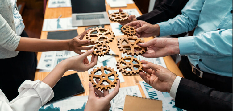 Group of multiracial business people joining gear wheels together over table as effective unity and productive teamwork concept. Efficient system business team process for solution solving. Meticulous