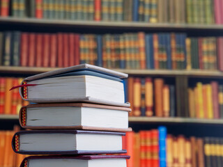 Stacks of books resting on a table with colorful shelves in the background