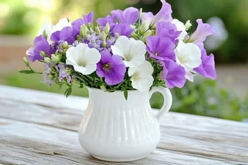 Delicate bouquet of wildflowers in muted lilac and green tones arranged in vintage vase on a rustic wooden table