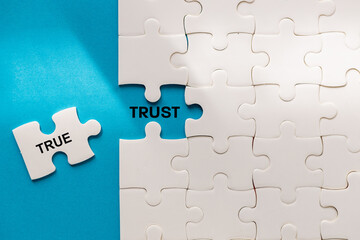 Obraz premium Symbol of true trust. The word TRUE from the puzzle reveals TRUST. Business concept. Truth and honesty builds trust. Blue background, copy space