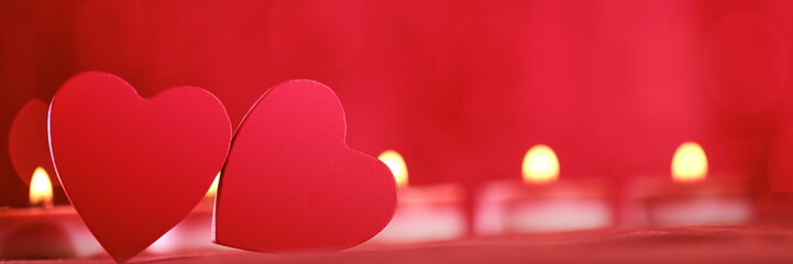 An intimate close-up of two red hearts in a beautifully blurred backdrop with flickering candle...