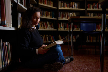 Woman reading a book while seated in a library surrounded by bookshelves