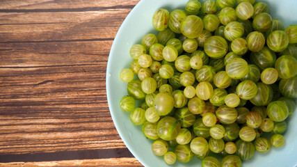 close up green gooseberry in blue plate on brown wooden background. summer berry . top view