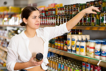 Young female customer diligently picking out tomato paste