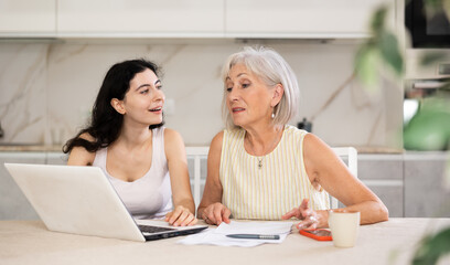 Elderly woman discussing deal with woman seller in kitchen at home