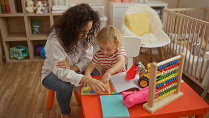 Mother and son enjoying playful learning on a colorful table in a cozy kindergarten bedroom, surrounded by toys and books, fostering love and growth indoors.