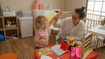 Mother and son clapping hands in cozy bedroom with toys, showcasing love and joy in an intimate indoor family setting, perfect for highlighting warm home environments.