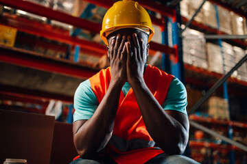 Stressed warehouse worker covering face with hands