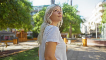 Attractive blonde woman standing outdoors in a city park during a sunny day