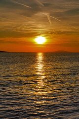 Sea horizon between dramatic sky with clouds and chem trails and shiny and wavy sea surface