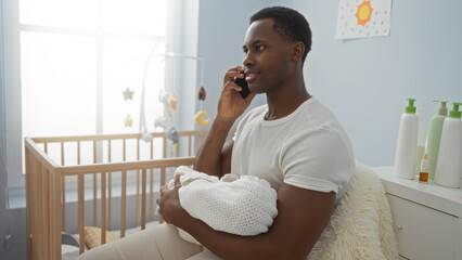 Young man holding baby in bedroom while talking on phone, showcasing nurturing fatherhood indoors in home setting, highlighting family care and communication