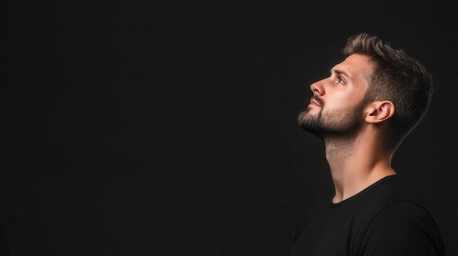 Young man looking up thoughtfully against a dark background in a contemplative pose with side profile view