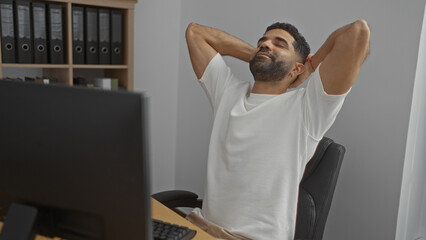 Young man relaxing in a modern office with files in the background, appearing calm and content at...