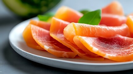 Fresh sliced grapefruit segments arranged on white plate with green leaf garnish, vibrant pink and orange citrus fruit close up for healthy eating.