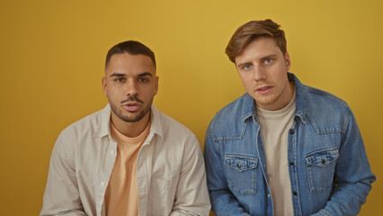 Handsome men friends posing together over isolated yellow background wall, looking into the camera with serious expressions.