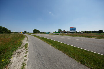 Open road stretches into distance under clear blue sky in rural landscape with grassy edges and billboards