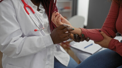 African american female doctor examining patient's wrist in a clinical setting, showcasing medical...